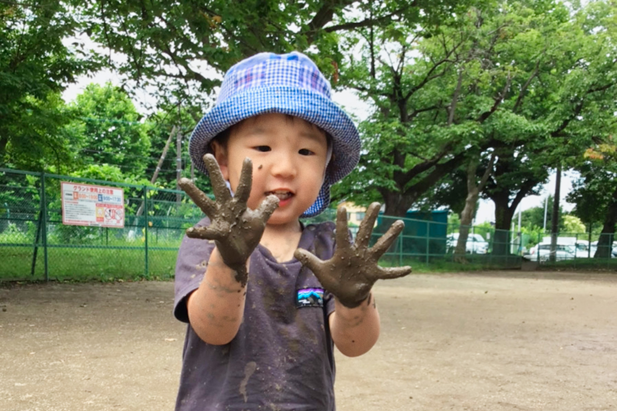 屋外で泥だらけの両手を見せている園児